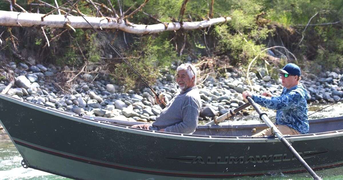Two individuals in a fishing boat, one holding a fishing rod while the other rows, surrounded by natural scenery.