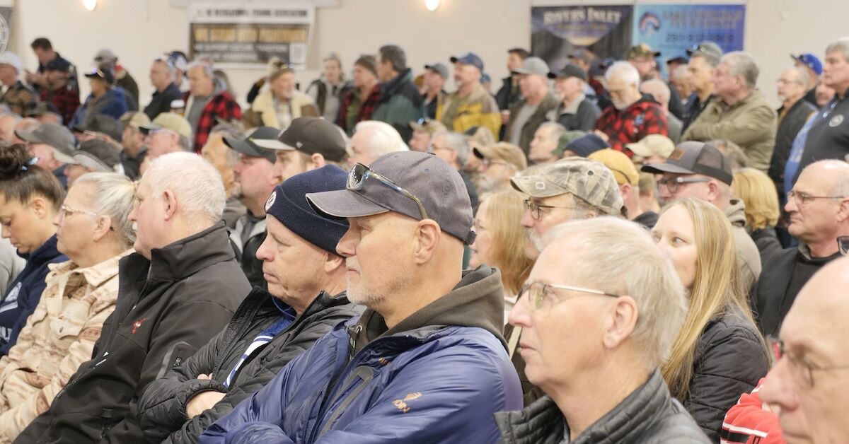 Crowd of people attending a town hall meeting, with individuals seated and focused on the speaker in a large indoor space.